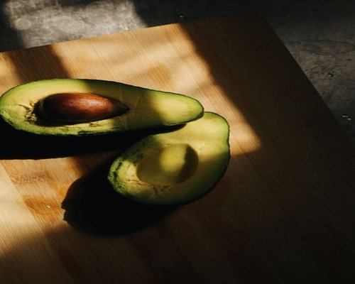 A top-down view of a modern kitchen counter with a cutting board, whole avocados, and bananas