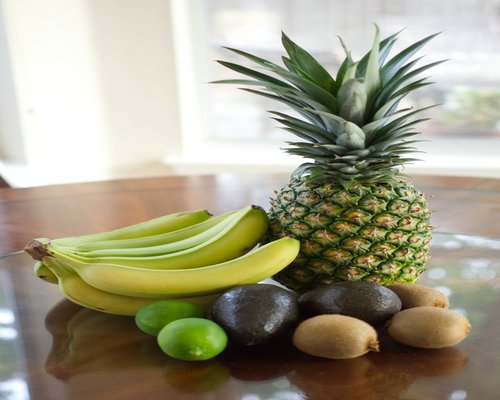 A collection of whole foods on a table including fresh avocados and tropical bananas